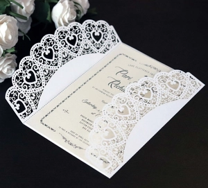 Macro view of laser-cut heart pattern on white wedding invitation sleeve with inner card