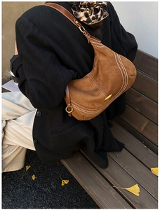 Detail of brown suede hobo bag featuring white contrast stitching and gold metal plate