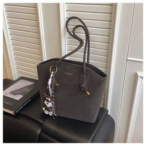 Detail shot of a dark brown suede tote bag with a Schnauzer charm and striped ribbon