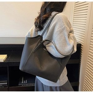 Detailed view of grey pebble leather tote bag worn by a model in a minimalist room