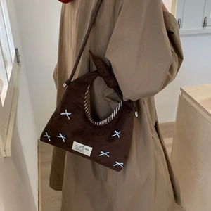 Detail view of brown suede dumpling bag with blue bows and knotted shoulder strap