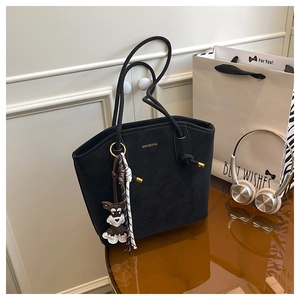 Detail of a black matte tote bag with golden logo and a cute schnauzer bag charm accessory