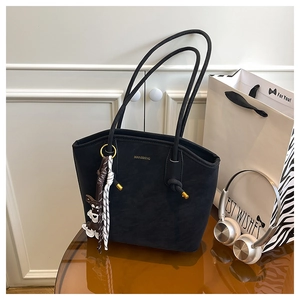 Detail of black textured tote bag with golden lettering and a cute dog charm on top