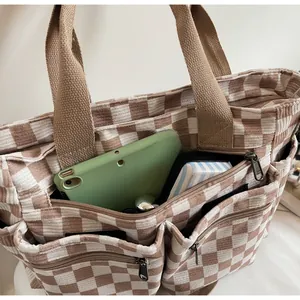 Detail of checkered corduroy tote bag showing multiple zipper pockets and storage capacity