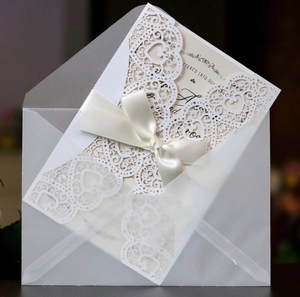 Detail of laser-cut heart wedding invitation with white satin ribbon and vellum envelope