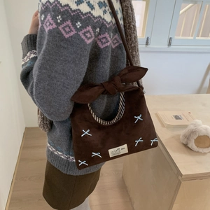 Detail of suede dumpling bag with blue bows and striped lining worn on the shoulder