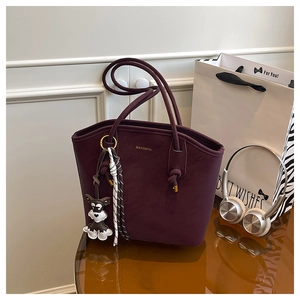 Detail of burgundy leather tote bag with gold logo, schnauzer charm and tassel