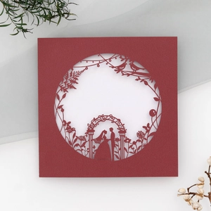 Macro detail of red square wedding card featuring laser-cut floral arch and romantic couple