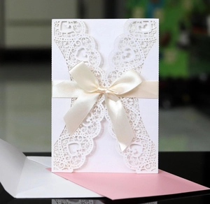 Elegant laser-cut wedding invitation in pearlescent white with a cream ribbon and envelope