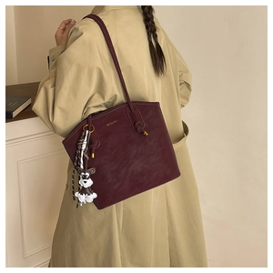 Close-up of wine red leather bucket bag with dog charm and plaid scarf on a tan trench coat