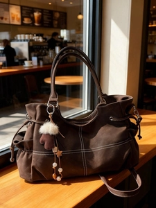 Brown suede tote bag with contrast stitching and decorative glove charm in a cafe