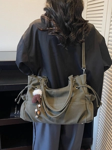 Dark green leather tote bag with white contrast stitching and tassel charm decoration