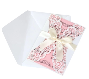 Detail of laser-cut heart pattern on white wedding invitation with a pink ribbon bow