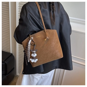 Detail of caramel tote bag with brand logo, long strap and cute dog leather charm