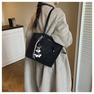 Detail view of black leather tote bag with silk scarf and dog charm on shoulder