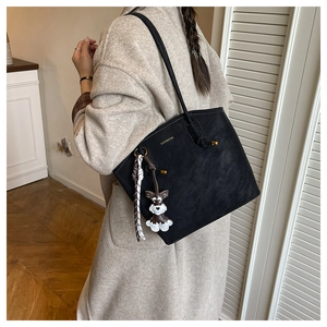 Detail of black textured bucket bag with dog charm and branded lettering on shoulder