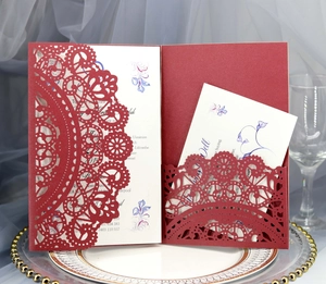 Detail of red laser-cut lace wedding invitation with floral insert on elegant dining plate