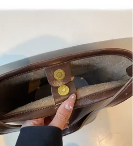 Close-up of golden magnetic buckle on dark brown leather bucket bag with gray lining