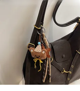 Close-up of a brown plush bear keychain with a birthday hat on a leather handbag