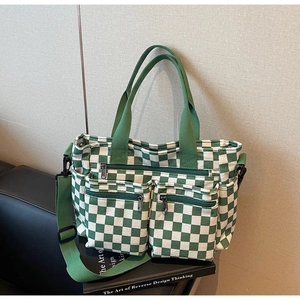 Detail of checkered canvas tote bag with triple zipper pockets and green strap