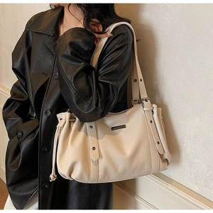 Détail de la texture cuir litchi crème et cordon latéral sur ce sac cabas élégant