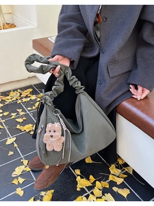 Detail of olive green leather tote bag with ruched handle and teddy bear charm accessory