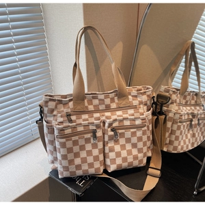 Detail of beige plaid canvas tote bag showing front zipper pockets and woven handles