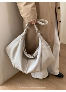 Close-up of white pleated leather tote bag showing lychee texture and silver metal hardware