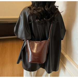 Detail of vintage red-brown leather bucket bag worn as a shoulder bag on a model