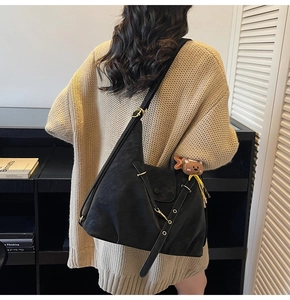 Detail view of black matte soft leather shoulder bag with cute brown bear plush charm