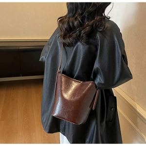 Detail of premium brown leather bucket bag with embossed text worn by a model