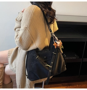 Detailed view of black textured tote bag featuring decorative straps and a plush bear charm