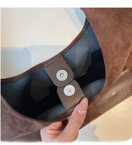 Detail of magnetic silver clasp and striped lining on dark coffee suede tote bag