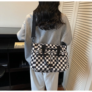 Detail of checkered canvas tote bag showing multiple zipper pockets and wide shoulder strap