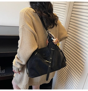 Detail of black suede tote bag with golden metal buckles and brown bear plush charm