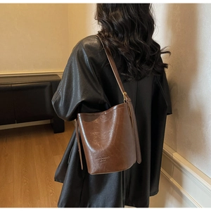 Brown leather bucket bag with adjustable strap and embossed text worn with a black jacket