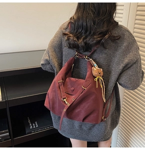 Detail of burgundy vintage tote bag with gold metal buckle and plush bear pendant detail