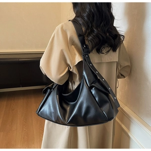 Vue détaillée d'un grand sac hobo noir avec œillets argentés porté sur un trench-coat beige