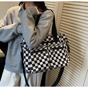 Close-up of checkerboard canvas tote bag featuring double front zipper pockets and strap