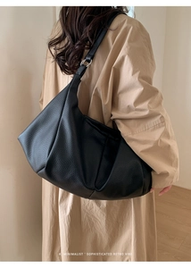 Detail of a large black lychee leather tote bag with retro pleats on a model's shoulder