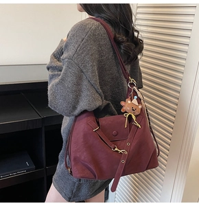 Detail view of burgundy leather tote bag with cute bear charm and adjustable strap on a model