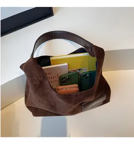 Close-up of a large brown suede tote bag interior filled with books, phones, and a wallet