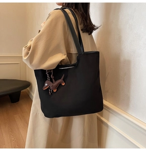 Détail du grand sac cabas noir avec breloque teckel marron sur trench-coat beige chic