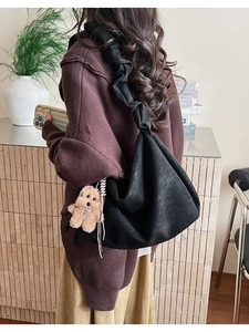 Black tote bag with wide pleated strap and brown bear charm worn by a model
