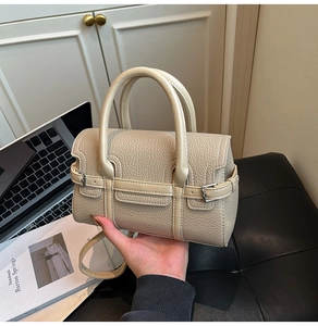 Detail der beigefarbenen Kieselleder-Handtasche mit Doppelgriffen und Metallschnallen