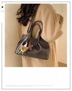 Détail du sac cabas plissé marron foncé avec breloque d'ours porté sur un manteau