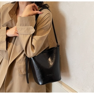 Close-up of black glossy leather bucket bag with embossed logo on khaki trench coat