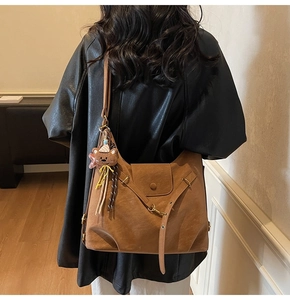 Brown vintage faux leather tote bag with cute bear pendant worn by model in black jacket