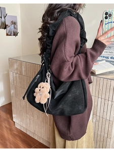 Detail of black hobo bag with pleated strap, side zipper, and brown teddy bear charm