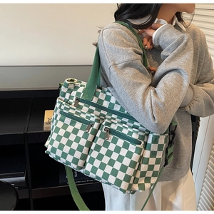 Detail of green checkerboard canvas tote bag featuring front zipper pockets and top handles